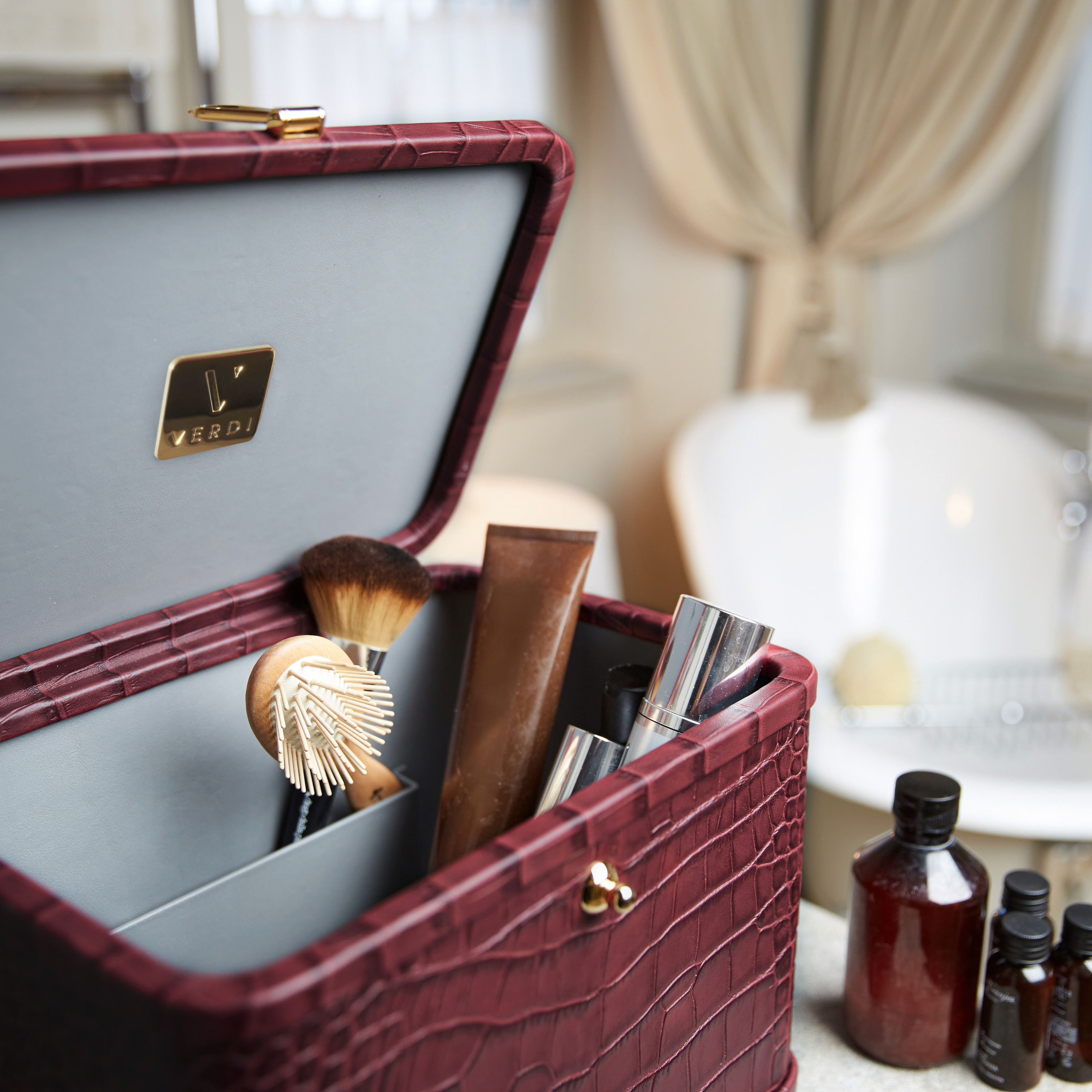 Verdi Livia large wine vanity case in crocodile print leather holding products in bathroom.